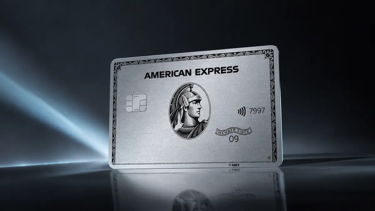 Cartão de metal prateado American Express Platinum em pé sobre superfície escura e espelhada, com feixes de luz