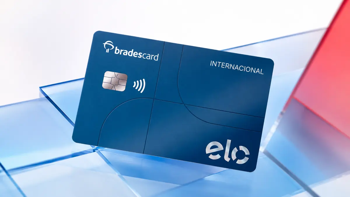 Cartão azul-escuro Bradescard Elo Internacional com chip prateado, apoiado em placas de vidro azuis e vermelhas