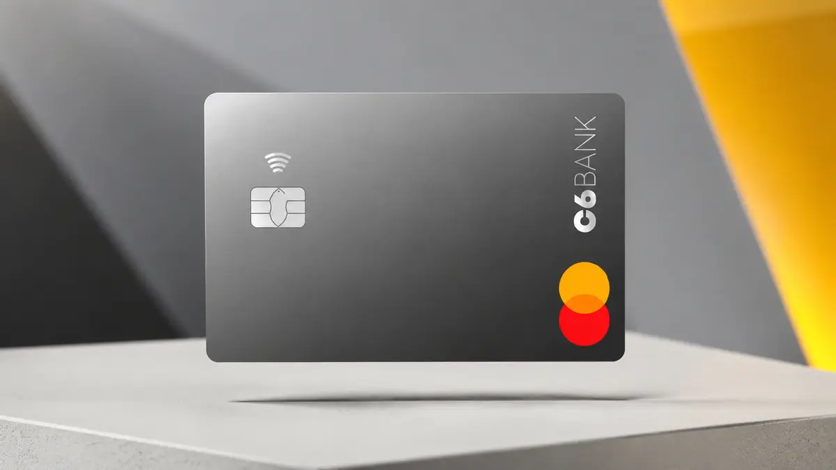 Cartão grafite do C6 Bank com chip prateado e os círculos laranja e vermelho da Mastercard, sobre base clara