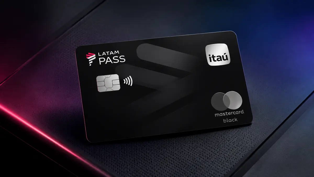 Cartão preto LATAM Pass Itaú com selo Mastercard Black, apoiado em superfície escura com reflexos azuis e rosa