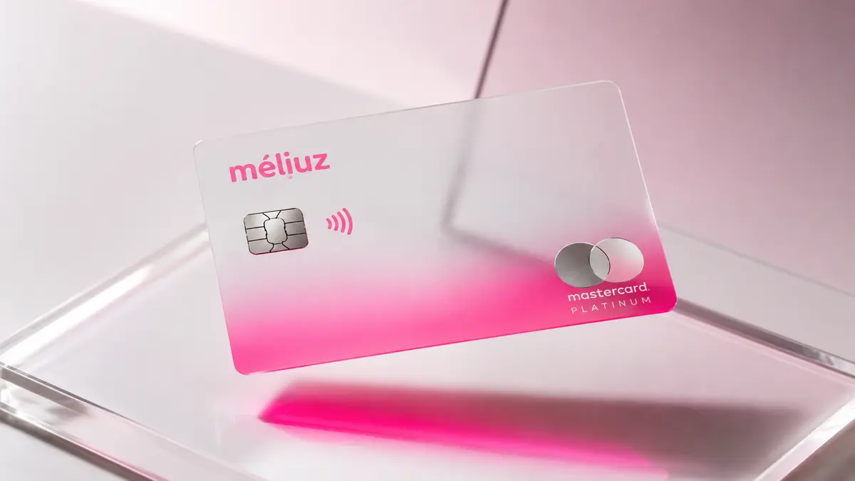 Cartão Méliuz translúcido em degradê branco e rosa, com logotipo méliuz e selo Mastercard Platinum, sobre vidro