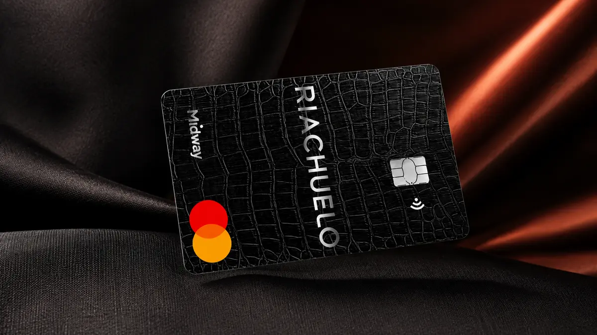 Cartão preto Riachuelo com textura de couro de crocodilo, marca Midway na lateral, chip e logo Mastercard, em tecido escuro
