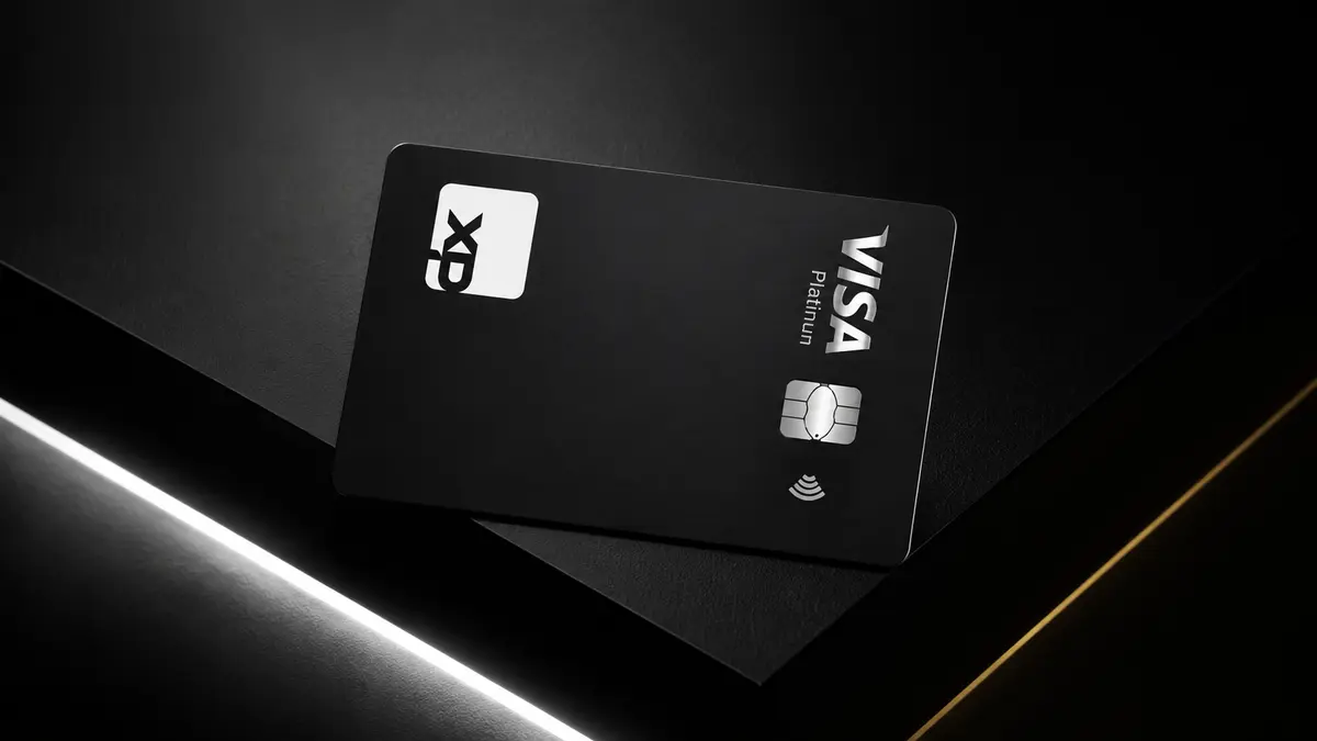 Cartão preto com o logo branco da XP, chip prateado e a marca Visa Platinum na lateral, sobre superfícies escuras