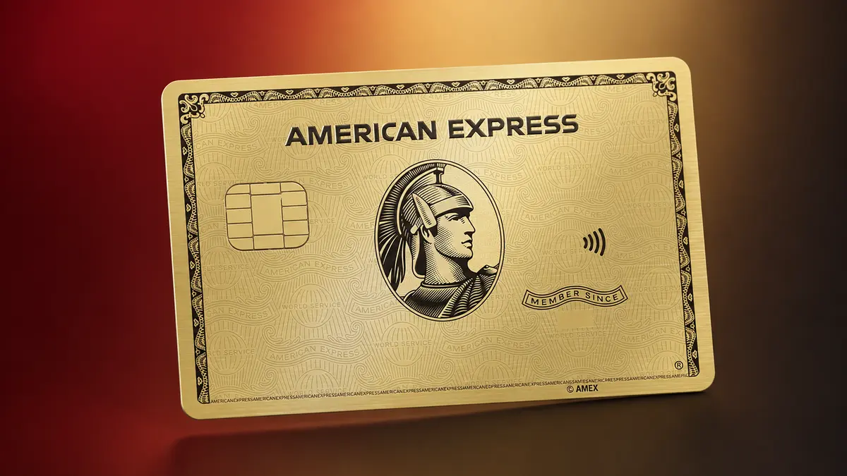 Tarjeta American Express dorada con el centurión grabado en el centro, sobre un fondo degradado de rojo a dorado