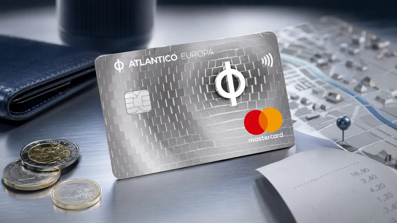Cartão prateado ATLANTICO Europa Mastercard junto a moedas de euro, mapa urbano e talão