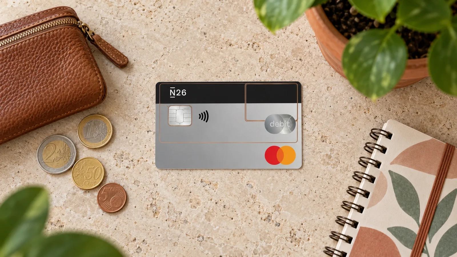 Cartão N26 Standard transparente junto a um porta-moedas e a um caderno sobre uma mesa.